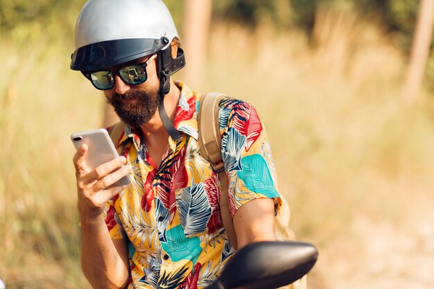 Homem bonito no capacete sentado na moto e usando telefone celular