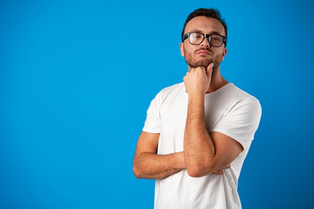 Homem bonito pensativo usando óculos contra fundo azul