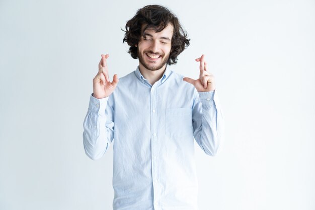 Homem bonito positivo, mostrando o gesto de dedos cruzados