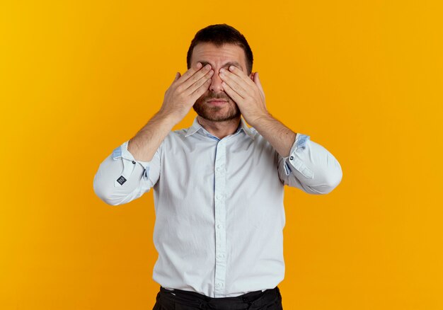 Homem bonito satisfeito fechando os olhos com as mãos isoladas na parede laranja