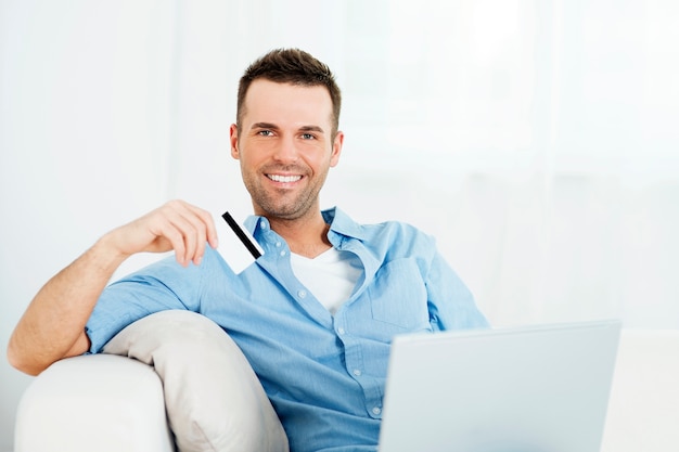 Homem bonito segurando cartão de crédito e usando laptop