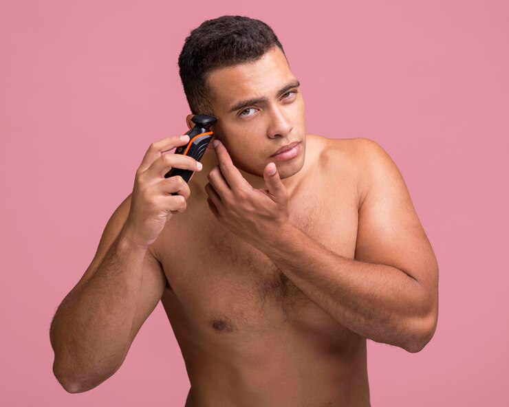 Foto grátis homem bonito sem camisa usando um barbeador elétrico