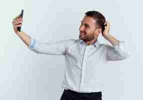 Foto grátis homem bonito sorridente coloca a mão na cabeça atrás olhando para o telefone isolado na parede branca