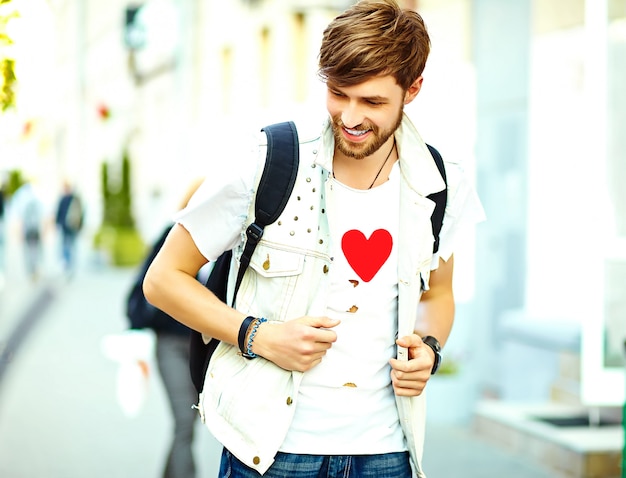 Homem bonito sorridente engraçado hipster em roupas de verão elegante posando na rua fundo