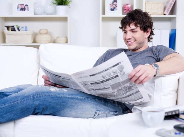 Homem bonito sorridente feliz lendo jornal em casa