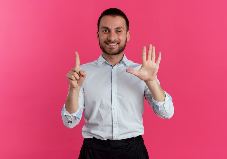 Foto grátis homem bonito sorridente gesticula seis com as mãos isoladas na parede rosa