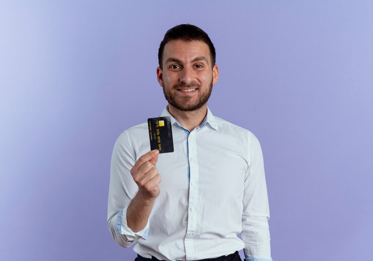 Foto grátis homem bonito sorridente segurando cartão de crédito isolado na parede roxa