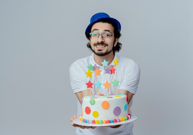 Foto grátis homem bonito sorridente, usando óculos e chapéu azul, segurando um bolo para a câmera, isolado no branco