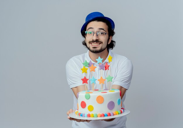 Homem bonito sorridente, usando óculos e chapéu azul, segurando um bolo para a câmera, isolado no branco