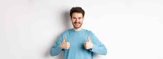 Foto grátis homem bonito sorrindo mostrando polegares para cima e aprovando boa escolha elogiando ou recomendando algo