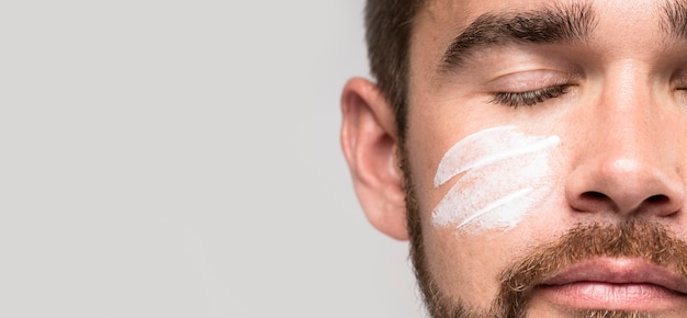 Homem bonito usando creme facial enquanto está de olhos fechados