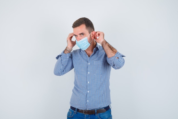 Homem bonito, usando máscara em camisa, jeans e olhando sério, vista frontal.