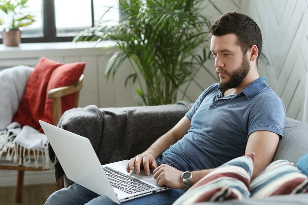 Homem bonito usando o laptop em casa. Conceito de teletrabalho