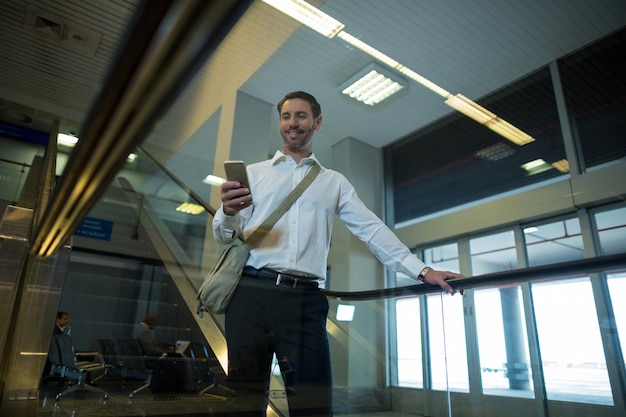 Homem bonito usando telefone celular na escada rolante