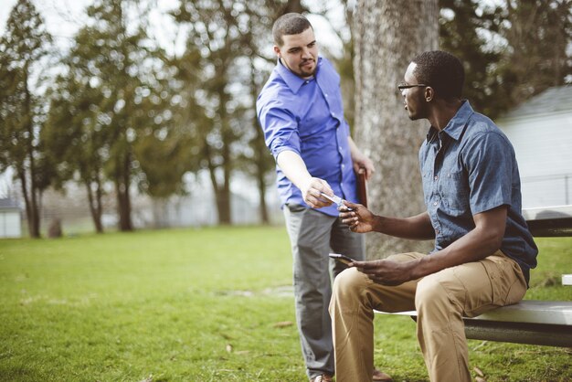 Homem branco dando um bilhete para um homem afro-americano no parque