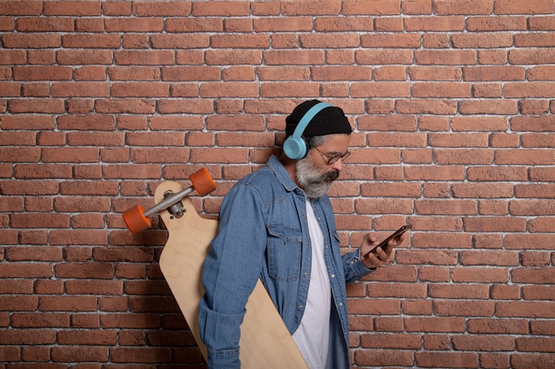 Homem branco segurando um skate enquanto usa seu smartphone