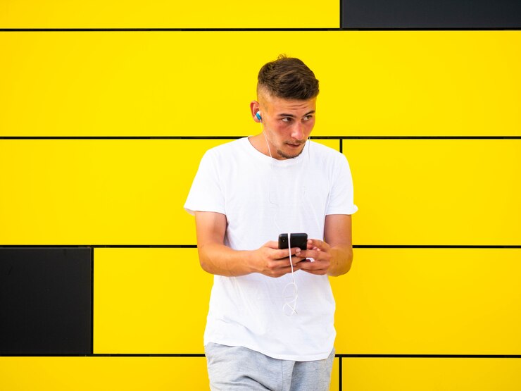 Foto grátis homem branco usando o telefone na parede amarela