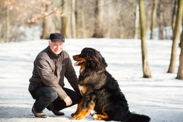 Homem brinca com um engraçado Bernese Mountain Dog na neve no parque