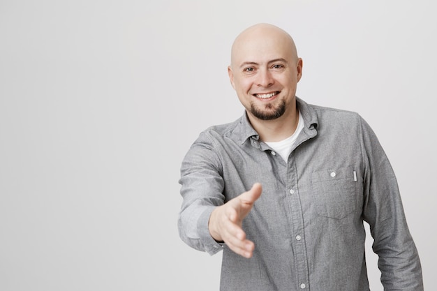 Homem careca adulto amigável dando a mão para um aperto de mão, sorrindo