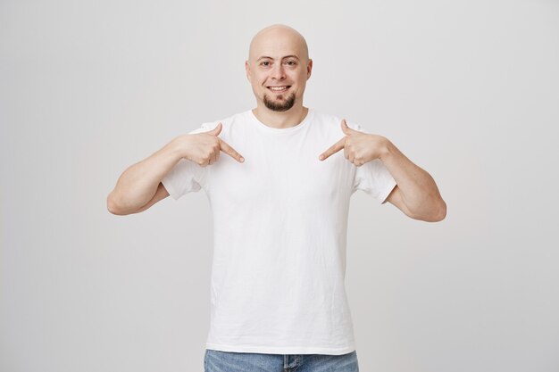 Homem careca barbudo sorridente feliz apontando para baixo