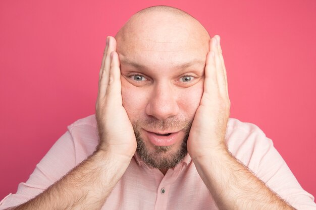 Foto grátis homem careca de meia-idade surpreso usando uma camiseta rosa e colocando as mãos no rosto