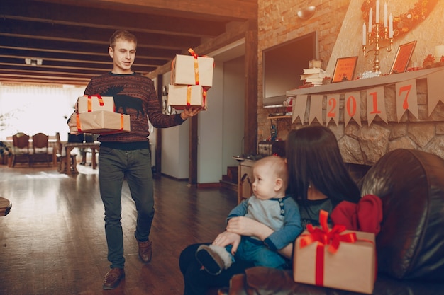 Homem carregando presentes, enquanto sua mulher está sentando-se com um bebê em um sofá