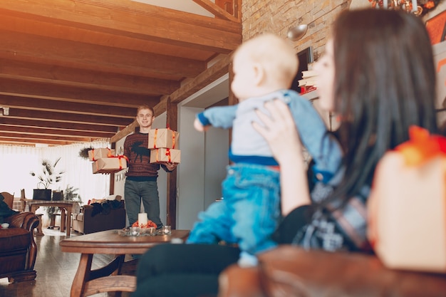 Homem carregando presentes, enquanto sua mulher está sentando-se com um bebê em um sofá