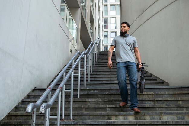 Homem carregando scooter elétrico nas escadas tiro completo