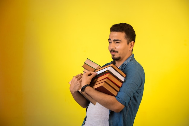 Homem carregando uma pilha de livros pesados com as duas mãos e sorrindo.