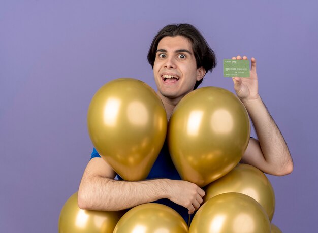 Homem caucasiano bonito animado com balões de hélio segurando um cartão de crédito