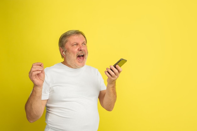 Homem caucasiano cantando com fone de ouvido e smartphone em amarelo