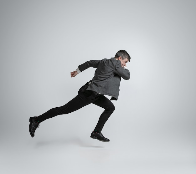 Homem caucasiano com roupa de escritório correndo isolado na parede cinza