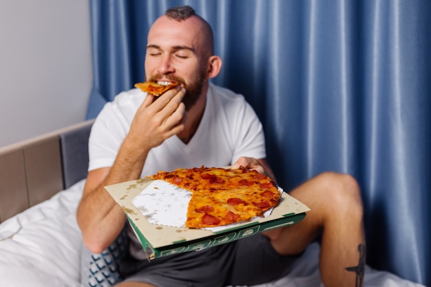 homem caucasiano comendo fast food em casa no quarto na cama