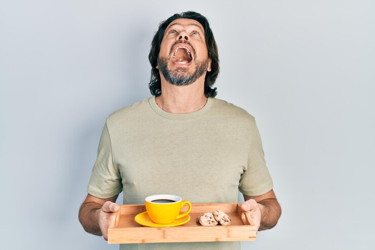 Foto grátis homem caucasiano de meia-idade segurando a bandeja de café da manhã com biscoitos e café zangado e bravo gritando frustrado e furioso gritando com raiva olhando para cima