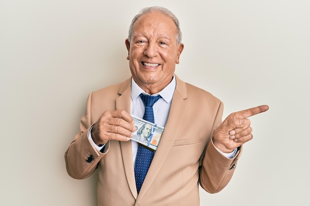 Homem caucasiano sênior economizando dinheiro suborno sorrindo feliz apontando com a mão e o dedo para o lado