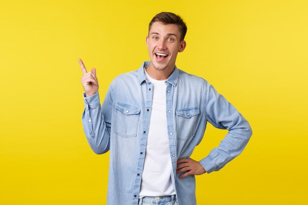 Homem caucasiano sorridente feliz alegre apontando o dedo no canto superior esquerdo e olhando a câmera encantada. Cara recomenda propaganda de produto, falando sobre ótima nova oferta, fundo amarelo.