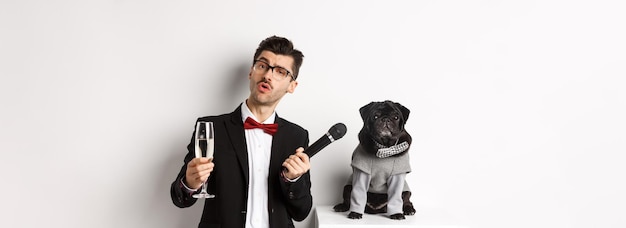 Homem chique bonito em copos levantando taça de champanhe e dando microfone para pug fofo na festa