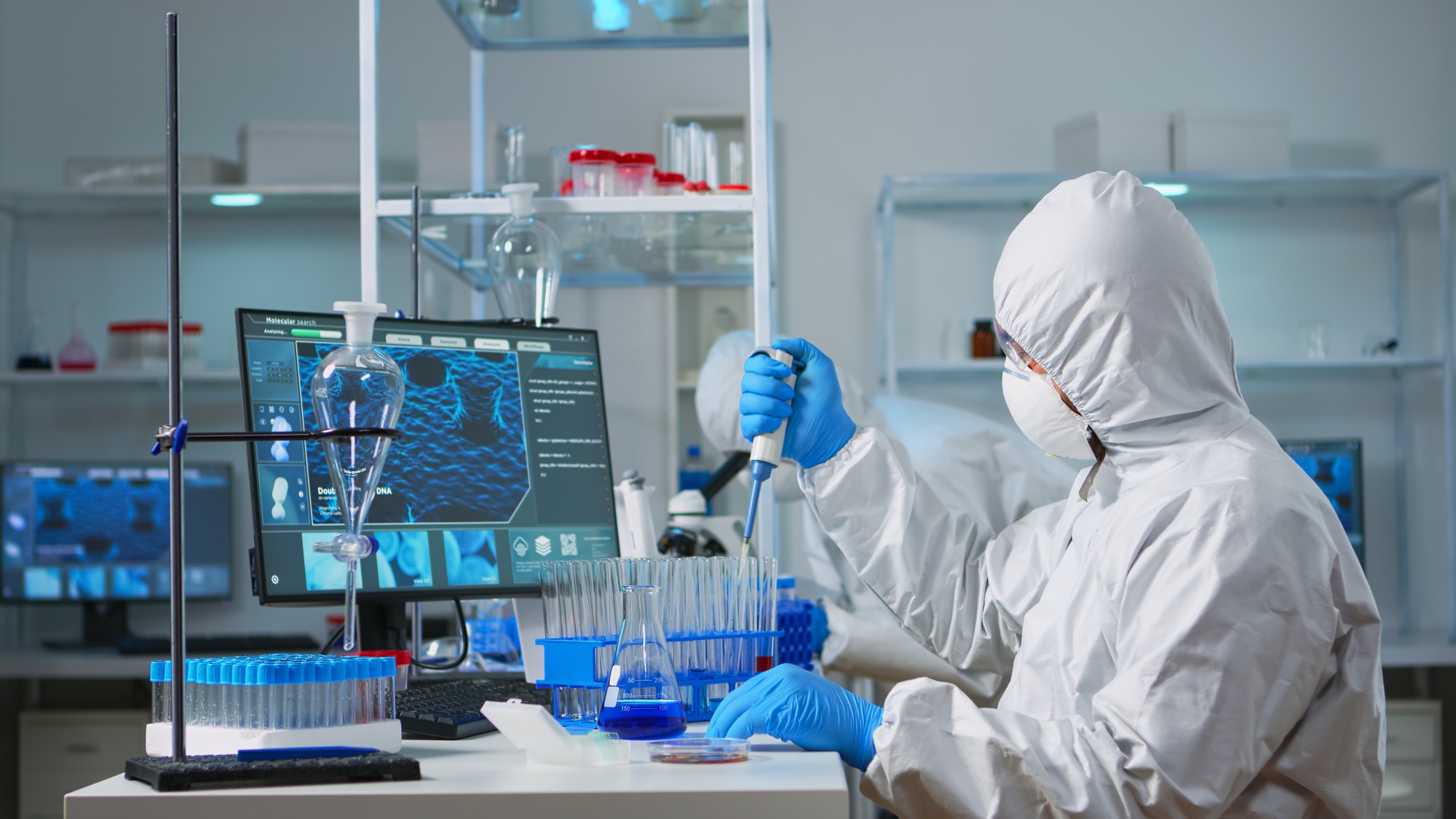 Homem cientista em macacão usando micropipeta em um moderno laboratório equipado. Equipe de médicos examinando a evolução da vacina com ferramentas de alta tecnologia e química para pesquisa no desenvolvimento do vírus covid19