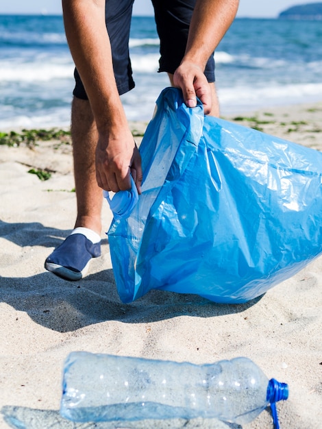 Homem coletando lixo plástico da praia e colocá-lo em sacos de lixo azuis para reciclagem