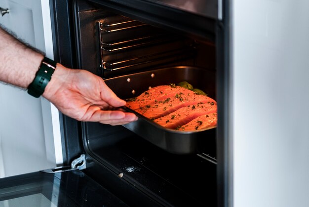 Homem colocando bife de salmão cru no forno