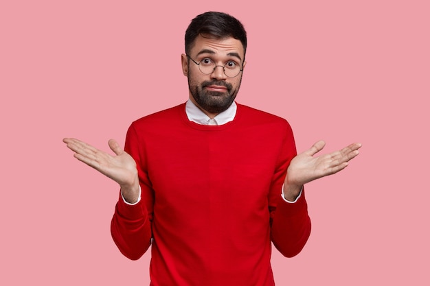 Foto grátis homem com a barba por fazer confuso e com cerdas escuras, espalha as palmas das mãos, sente-se inseguro, olha com desprazer