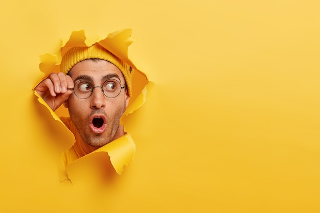 Foto grátis homem com a barba por fazer espantado olhando pelo buraco no papel amarelo