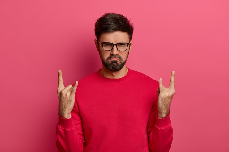 Foto grátis homem com a barba por fazer insatisfeito e sombrio fazendo gesto de rock n roll