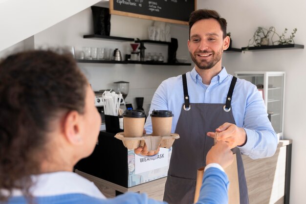 Homem com avental oferecendo comida para viagem embalada para uma cliente