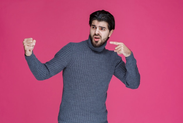 Homem com barba apontando para algo ou apresentando alguém.