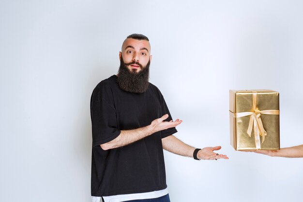 Homem com barba, mostrando sua caixa de presente envoltório dourado.