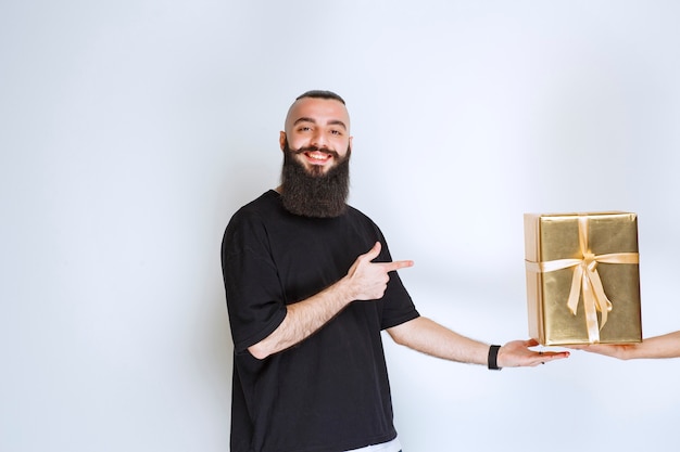 Homem com barba, mostrando sua caixa de presente envoltório dourado.