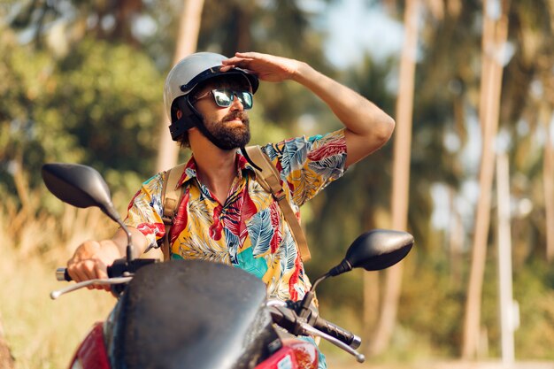 Homem com barba na camisa tropical colorida, sentado na moto