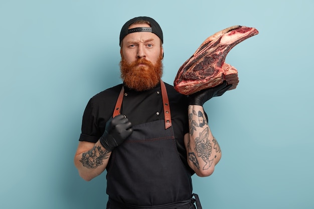 Homem com barba ruiva usando avental e luvas segurando carne