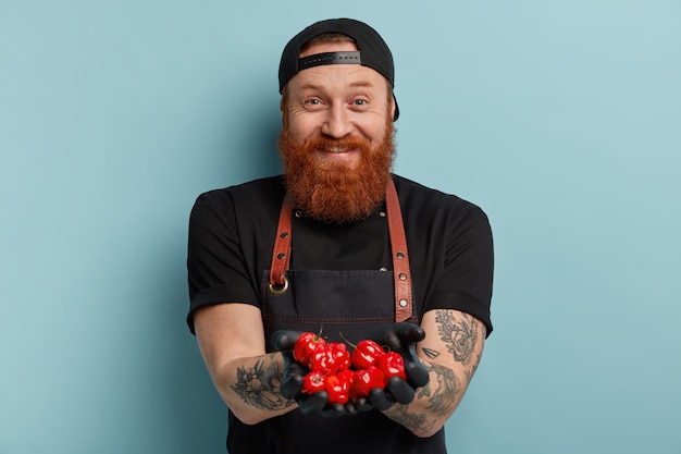 Homem com barba ruiva usando avental e luvas segurando tomates